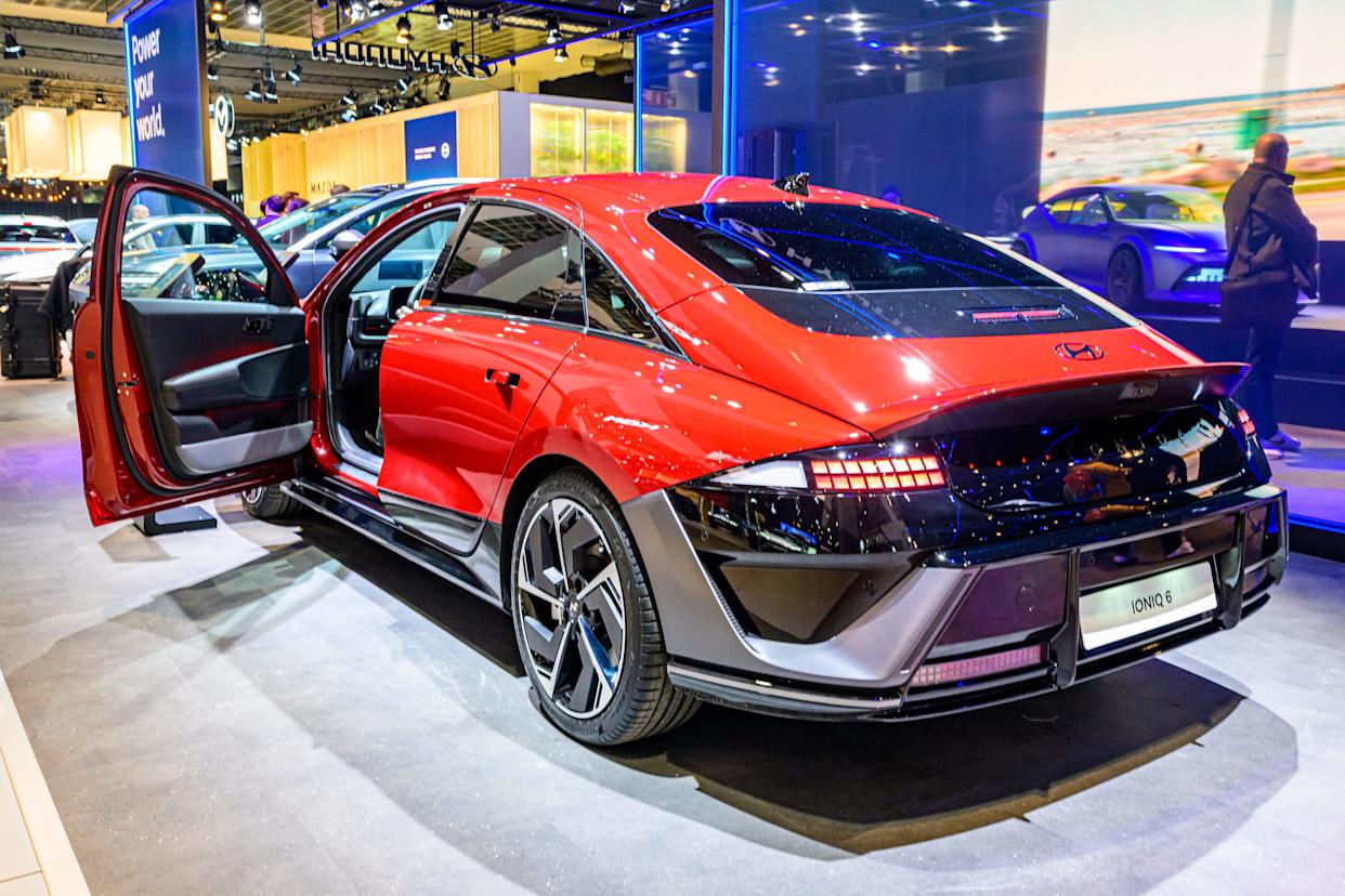 Un Hyundai Ioniq 6 Standard rojo está estacionado en el piso de una sala de exposición. Se abre la puerta del conductor y se abren las manijas.