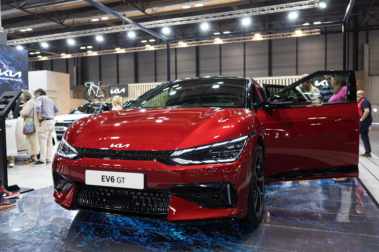 Un Kia EV6 GT rojo está estacionado en el piso de la sala de exhibición con los faros encendidos y la puerta del lado del conductor abierta.