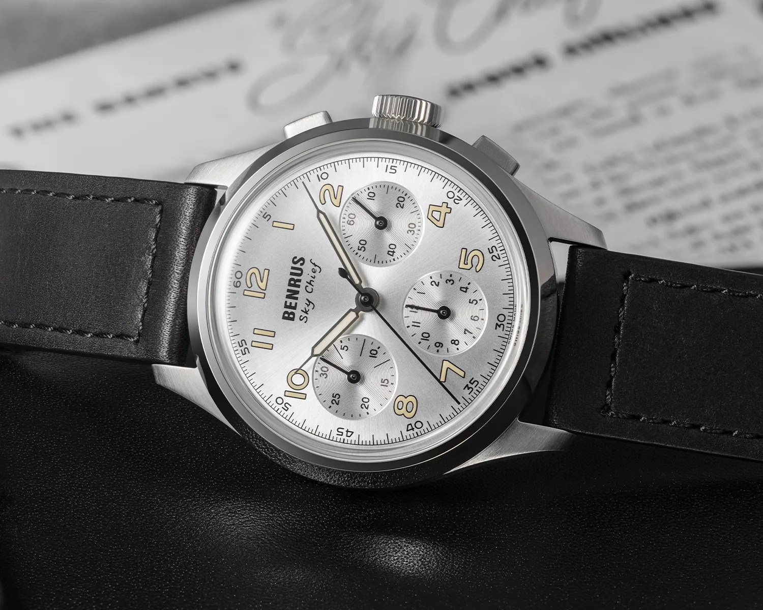 Reloj cronógrafo Benras Sky Chief plateado con correa de cuero negro sobre superficie negra.