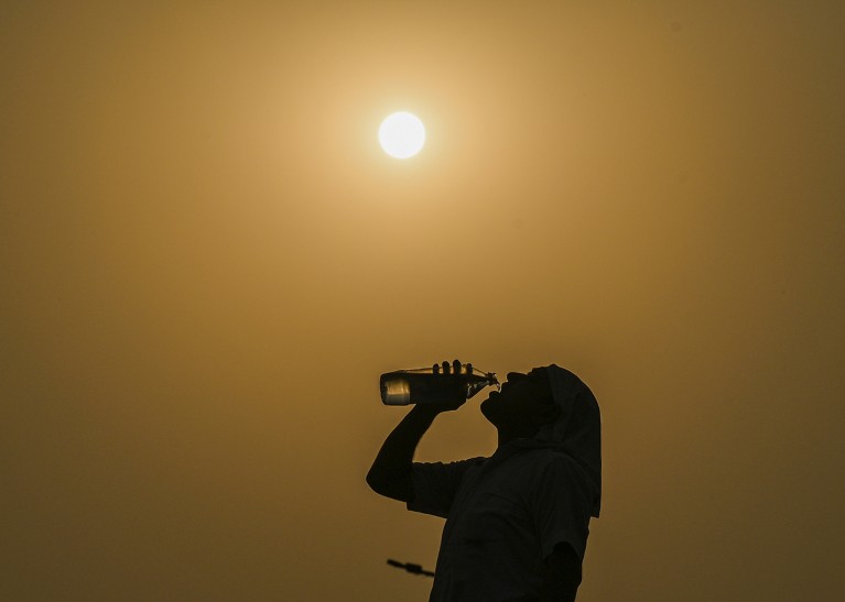 Un hombre bebe agua de una botella en un día oscuro y caluroso mientras la temperatura aumenta y el sol es completamente visible en el fondo.