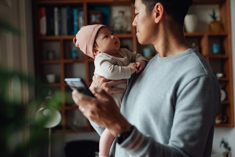 Un hombre asiático con una sudadera gris le sonríe a un niño mientras sostiene un teléfono