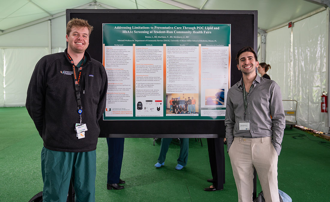 Dos estudiantes de medicina se encuentran junto a un cartel de investigación en la Conferencia de Liderazgo en Salud Comunitaria del DOCS, presentando los hallazgos de una iniciativa de salud basada en la comunidad.