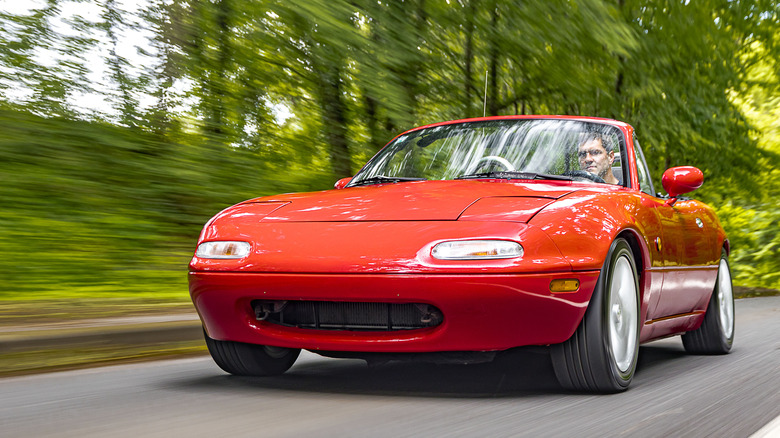 Rojo NA Mazda Miata en Forest Road, vista frontal 3/4