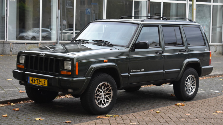Jeep Cherokee XJ estacionado en la carretera, vista frontal 3/4, exterior verde muy oscuro, placas holandesas