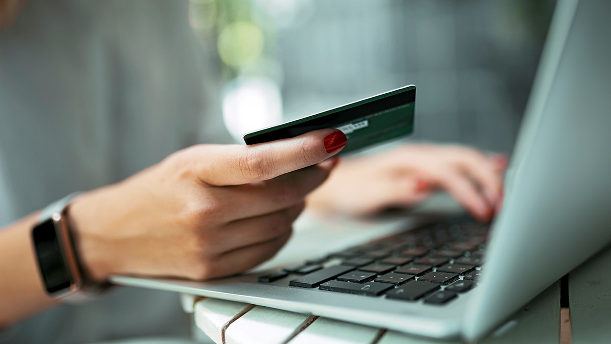 Una mujer sosteniendo una tarjeta de crédito junto a una computadora portátil abierta