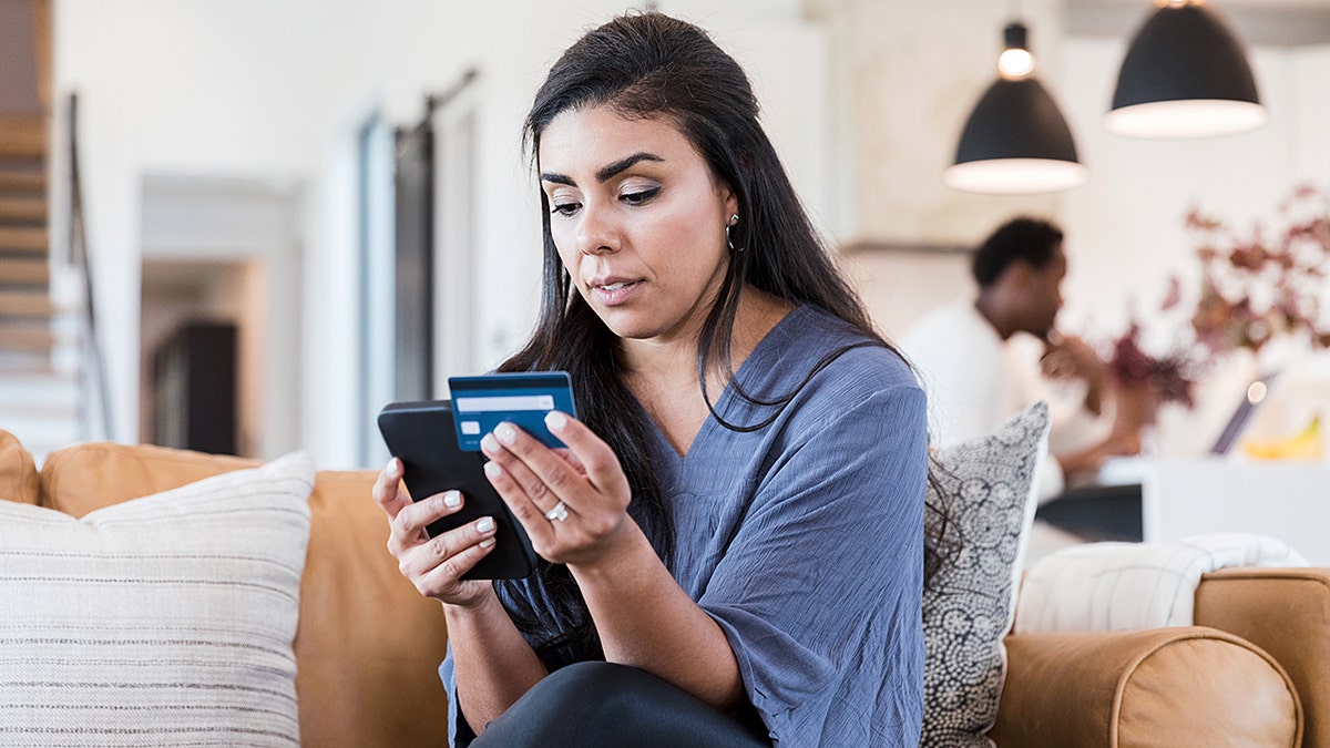 Mujer seria ingresando información de tarjeta de crédito por teléfono mientras compra en línea